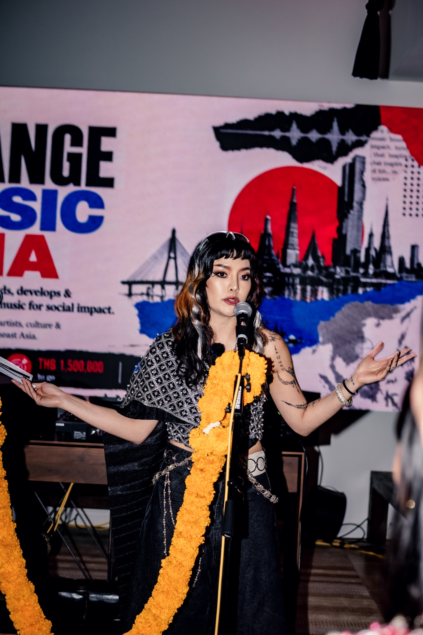 Pyra speaking at a Change Music Asia event in front of the organization’s Bangkok artwork